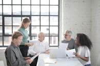 Group of diverse colleagues in casual wear brainstorming together at table with laptop while working with papers in creative office workspace